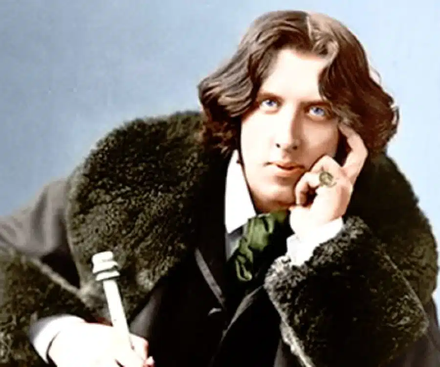 Oscar Wilde, a brown haired man stares directly at you with blue eyes, one hand on his face